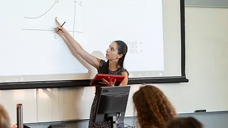 Professor at the front of a classroom teaching calculus equations.